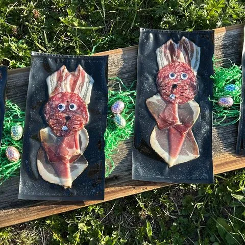 Vakuumierte Osterhasen aus Aufschnitt auf einem Holzbrett im Gras